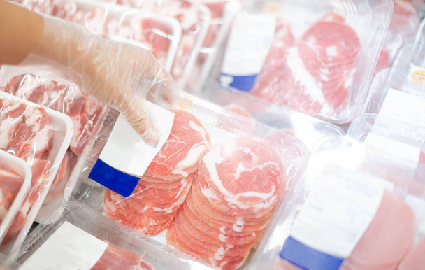 O funcionário do supermercado preparando a fatia de carne de porco fresca na bandeja de exibição para os consumidores selecionarem em um supermercado
.  - Fotografia, imagem