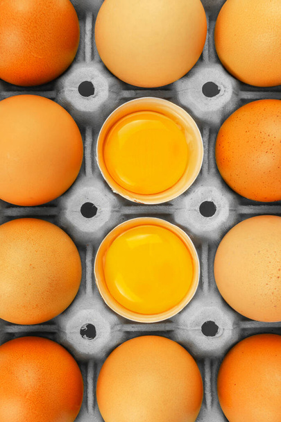 Brązowe pudełko na jaja kurze z 2 otwartymi i widocznymi żółtkami jaj w szarym opakowaniu - Zdjęcie, obraz