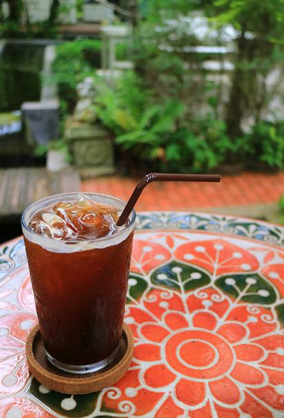夏の庭のテーブルの上に氷のコーヒーのガラス、背景を赤らめる - 写真・画像