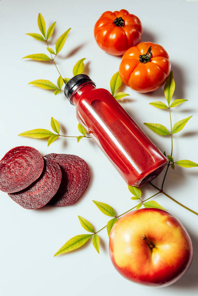 Bebida de batido rojo en botella cerca de manzanas maduras tomates y remolachas. Dieta de desintoxicación para el cuerpo y la mente sanos. concepto de alimentos saludables. Sobre fondo claro - Foto, imagen