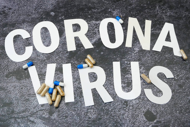 Coronavirus kelimesi harflerden ve siyah arkaplandaki haplardan geliyor. - Fotoğraf, Görsel