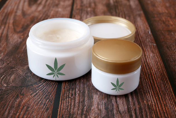 Cannabis-Creme-Kosmetik in Dosis mit Marihuana-Pflanze auf hölzernem Hintergrund. Cannabis-Kosmetikkonzept. - Foto, Bild