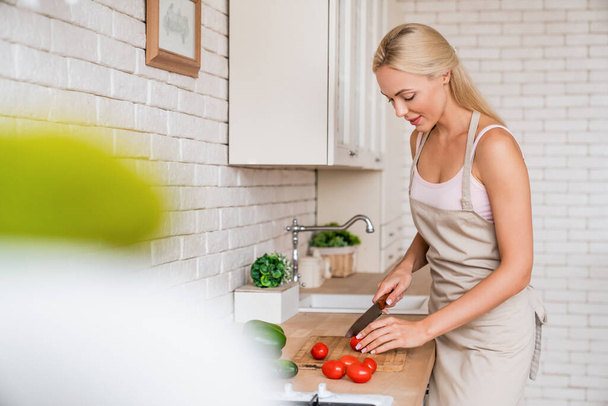 Fiatal nő vágás zöldségek a konyhában otthon - Fotó, kép
