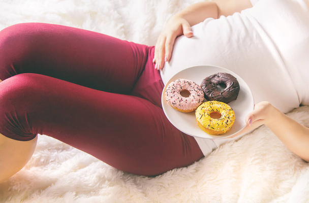 Eine schwangere Frau isst süße Donuts. Selektiver Fokus. Lebensmittel. - Foto, Bild