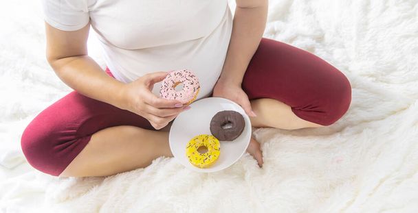 Una donna incinta mangia ciambelle dolci. Concentrazione selettiva. Alimenti. - Foto, immagini