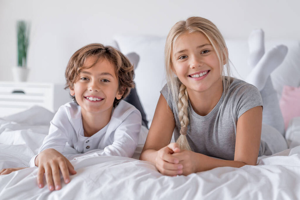 Happy time concept. Brother and sister lying in bed at the morning and smiling in camera - Foto, Bild