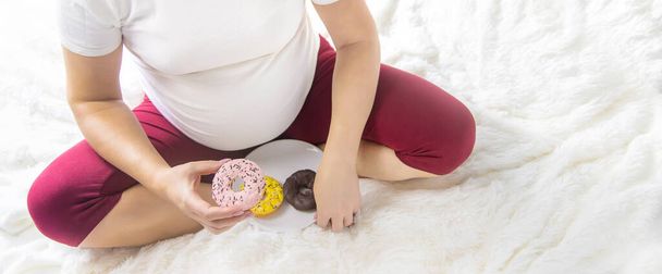 Une femme enceinte mange des beignets sucrés. Concentration sélective. Produits alimentaires. - Photo, image