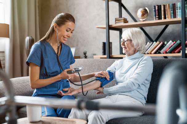 Nurse measuring blood pressure of elderly woman indoors - Фото, изображение
