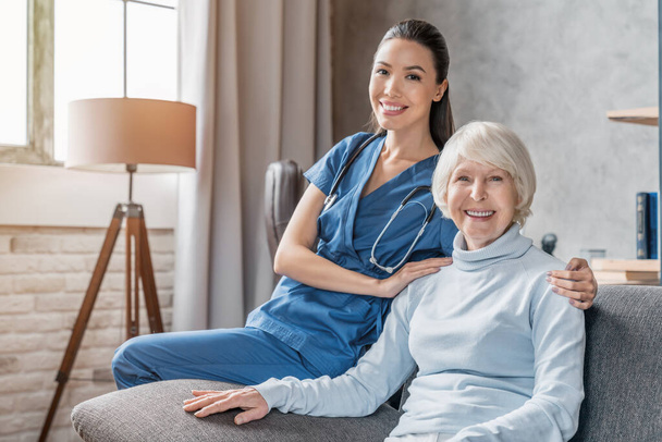 Portrait of happy elderly woman with nurse at home - Photo, image