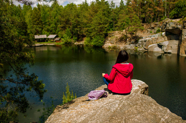 Nuori aikuinen aasialainen nainen, jolla on reppu kivellä, joka ihailee järven näkymää syksyllä. - Valokuva, kuva