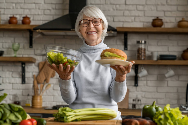 Senior woman making choice between healthy and junk food - Photo, Image