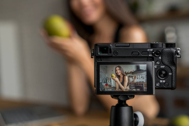 Young female blogger on camera screen holding mango for healthy eating vlog - Фото, изображение