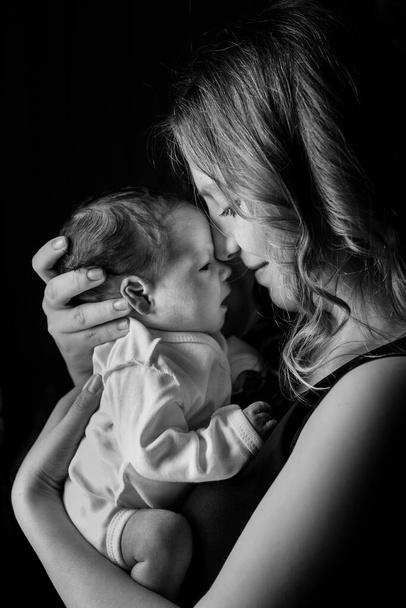 Černobílá fotografie novorozence na izolovaném černém pozadí jeho matky. Zdravotní péče a lékařská láska životní styl matka. - Fotografie, Obrázek