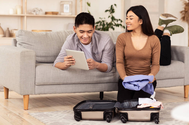 Szczęśliwa para Korzystanie z komputera typu tablet Pakowanie siedzi z walizką w pomieszczeniu - Zdjęcie, obraz