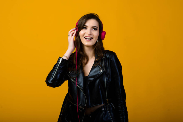 Mujer joven con auriculares escuchando música y sintiéndose feliz en el fondo amarillo del estudio - Foto, imagen