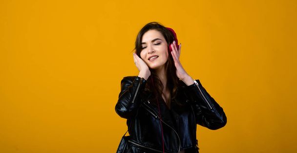 Mujer joven con auriculares escuchando música y sintiéndose feliz en el fondo amarillo del estudio - Foto, Imagen