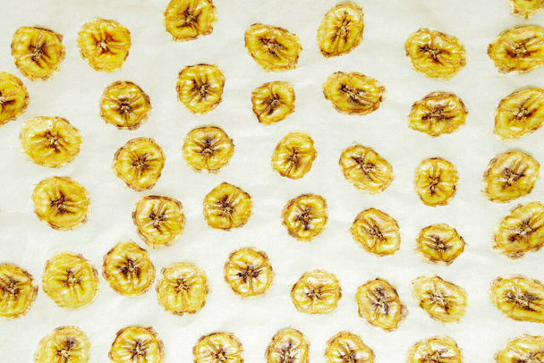 Bananowe chipsy, plasterki świeżych dojrzałych bananów jako tło żywności. gotowanie na pergaminie w domu - Zdjęcie, obraz