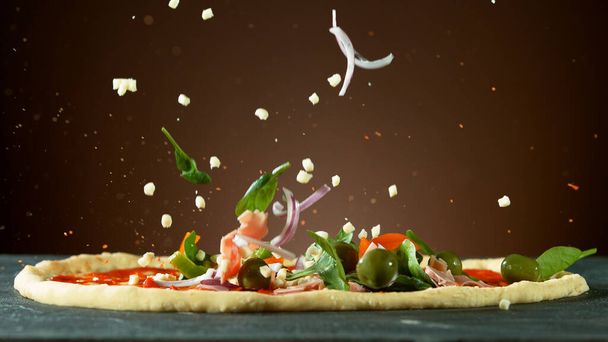 Falling raw ingredients on pizza, freeze motion. Italian traditional meal. - Photo, image