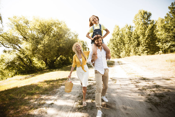 自然と一緒に歩く陽気な両親と小さな娘 - 写真・画像