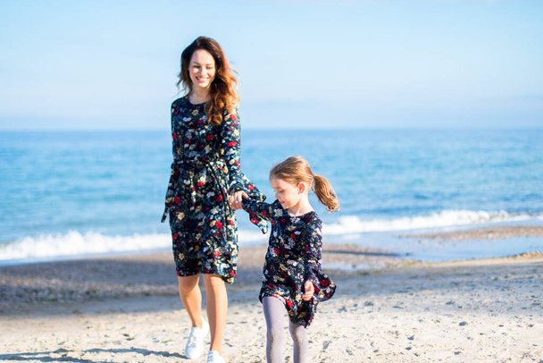 a little girl leads by the hand her mother on the beach. similar dresses - Foto, immagini