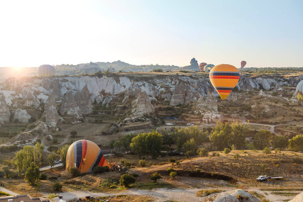 Goreme, Kapadokya, Türkiye 23 Ağustos 2019: Birçok sıcak hava balonu iniyor. İnsanlar onlara yerden bakıyorlar. Kapadokya Dünya Piramitleri. Turizm konsepti. - Fotoğraf, Görsel