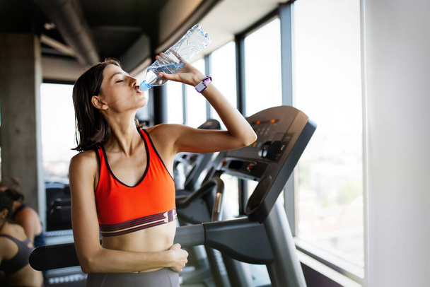 Refreshing after workout. Beautiful young woman drinking water to stay hydrate in gym - Photo, image