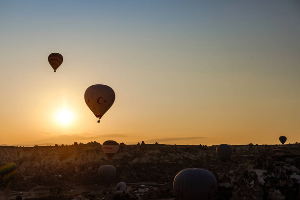 Goreme, Cappadocia, Turkey 23 August 2019: Many hot air balloons in sky. People look at them from the ground. Cappadocia Earth Pyramids. Tourism concept. - Фото, изображение