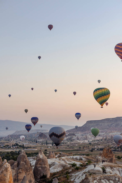 Goreme, Cappadocia, Turkey 23 August 2019: Many hot air balloons in sky. People look at them from the ground. Cappadocia Earth Pyramids. Tourism concept. - Fotografie, Obrázek