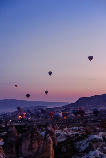 Goreme, Cappadocia, Turchia 23 agosto 2019: Molte mongolfiere in cielo. La gente li guarda da terra. Piramidi della Cappadocia. Concetto turistico
. - Foto, immagini