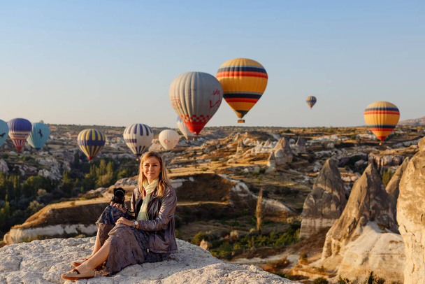 Goreme, Cappadocia, Turkey 23 August 2019: Beautiful blonde woman photographer takes pictures of flying hot air balloon at dawn in Cappadocia, Turkey. Travel concept.   - Foto, Imagem