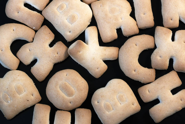 Маленьке солодке печиво у вигляді букв латинського алфавіту на чорному тлі макрофотографія. - Фото, зображення