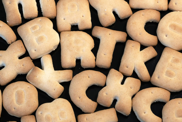 Pequeñas galletas dulces en forma de letras del alfabeto latino sobre un fondo negro foto macro de cerca
 - Foto, imagen