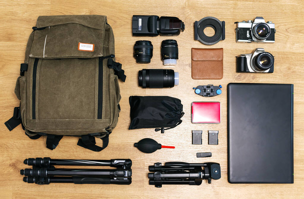 Ahşap bir masa üzerinde profesyonel fotoğraf ekipmanlarının üst görünümü (kameralar, lensler, tripodlar, dizüstü bilgisayarlar, sırt çantası, aksesuarlar...) - Fotoğraf, Görsel