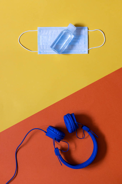 Maqueta vertical, auriculares azules en dos colores de fondo amarillo y naranja, gel hidroalcohólico y mascarilla, espacio de copia
 - Foto, imagen