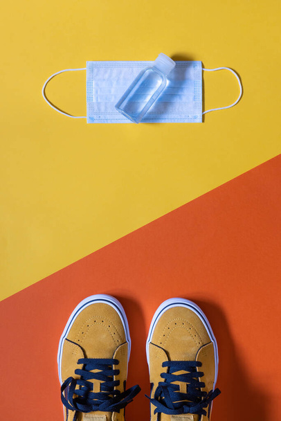 vertical mockup, mustard colored shoes on two colors yellow and orange background , hydroalcoholic gel and face mask, copy space - Photo, Image