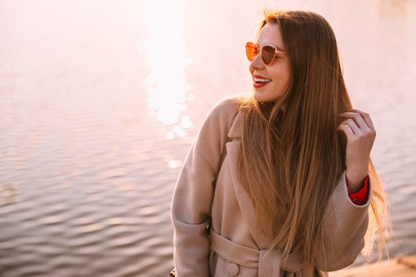 Muotokuva nuori hymyilevä tyttö takki taustalla järven auringonlaskun aikaan - Valokuva, kuva