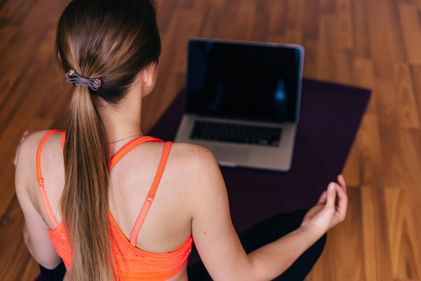 Menina fitness fazendo ioga em casa ao usar o computador. Mulher esportiva bonita praticando yoga medita - Foto, Imagem