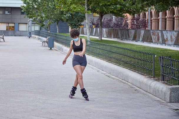 Latin girl skating on inline skates protecting herself with a face mask - Fotografie, Obrázek