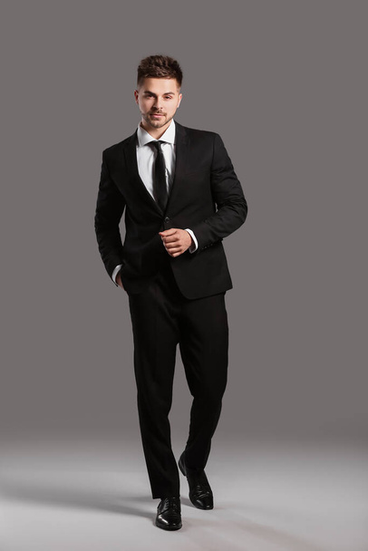 Όμορφος νεαρός με κομψό κοστούμι σε γκρι φόντο - Φωτογραφία, εικόνα