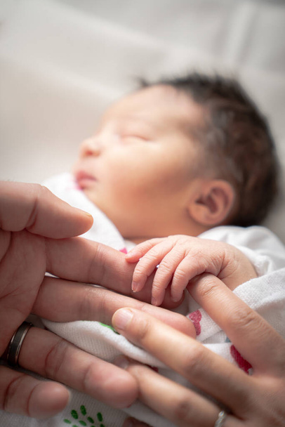 Une petite fille nouveau-née dans une lange de couverture enroule sa petite main et ses doigts autour des doigts de son père et de sa mère pendant qu'elle dort paisiblement
. - Photo, image