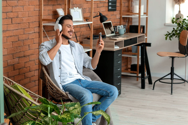 Knappe jongeman die thuis naar muziek luistert - Foto, afbeelding