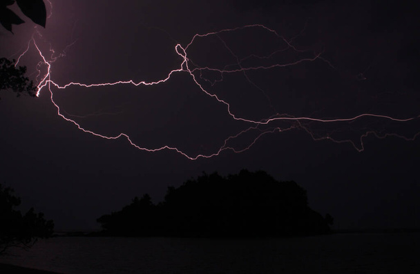 Inselsilhouette und Blitz bei nächtlichem Sturm. Fast schwarzes Nachtbild mit elektrisierenden Gewitterlichtern - Foto, Bild