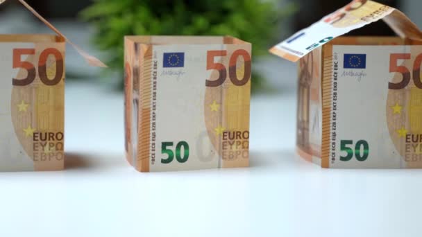 ユーロ紙幣で作られた3つの小さな家モデル、人間の手は紙屋根の建設フレームをカバーしています。紙幣資産への投資、建設業株式の金融取引 - 映像、動画