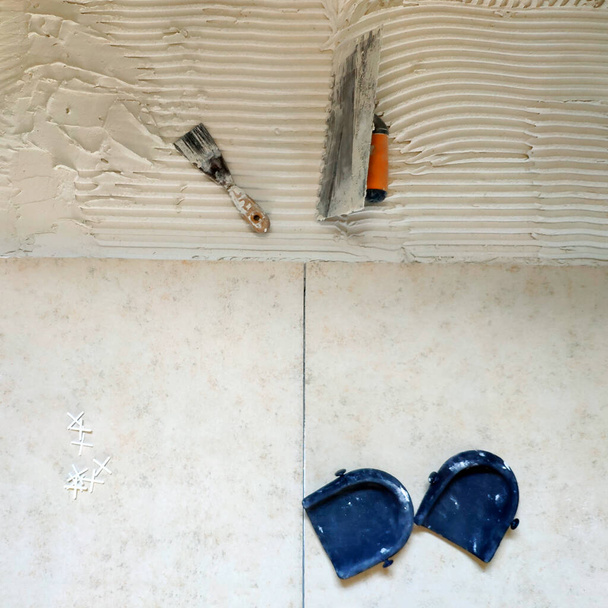 Installation of  ceramic tiles. Tools for laying tiles- trowel, toothed spatula, plastic crosses, knee pads. Glue for a tile with a gear pattern.  Renovation or repair concept. - Photo, Image