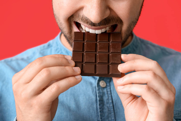 Przystojny młody człowiek ze smaczną czekoladą na tle koloru, zbliżenie - Zdjęcie, obraz