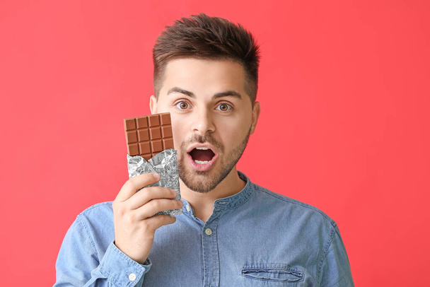 Yllättynyt nuori mies, jolla on maukas suklaa väritaustalla
 - Valokuva, kuva