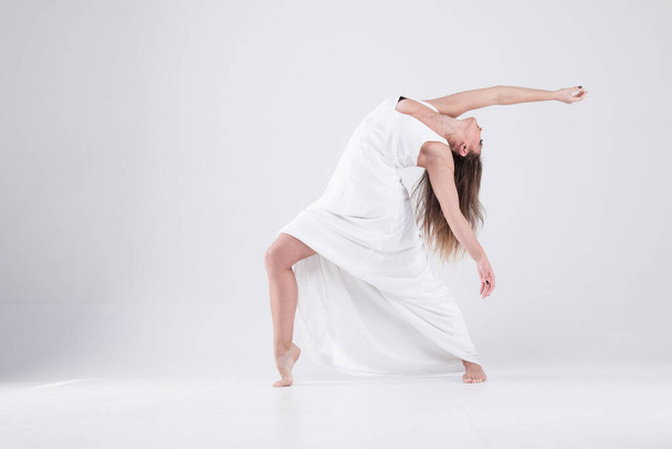 Κορίτσι σε χορευτική πόζα με λευκό φόρεμα. Γυναίκα με λευκό σέξι κορίτσι με λευκό φόρεμα. Ευελιξία, μοντέρνο, stretching, κλασικό, κομψό, στυλ - Φωτογραφία, εικόνα