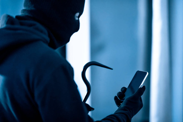 Villain holding crowbar and smartphone preparing burglary - Photo, Image