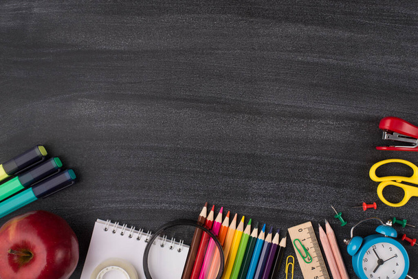 Okuma ve okul konsepti. Üst tepedeki renkli kırtasiyenin resmi ve metin için boş yeri olan karatahtaya izole edilmiş bir elma - Fotoğraf, Görsel
