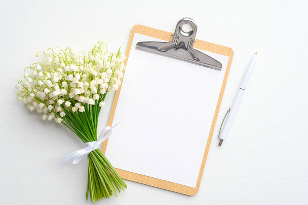 Wedding to do list concept. Clipboard with blank paper note, lily of the valley and pen on white background. Flat lay, top view. - Fotó, kép